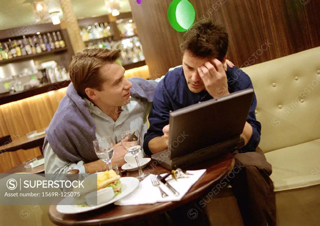 Two men at cafe table, one with laptop computer