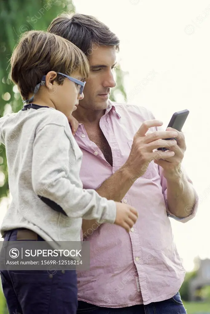 Father and young son looking at smartphone together outdoors