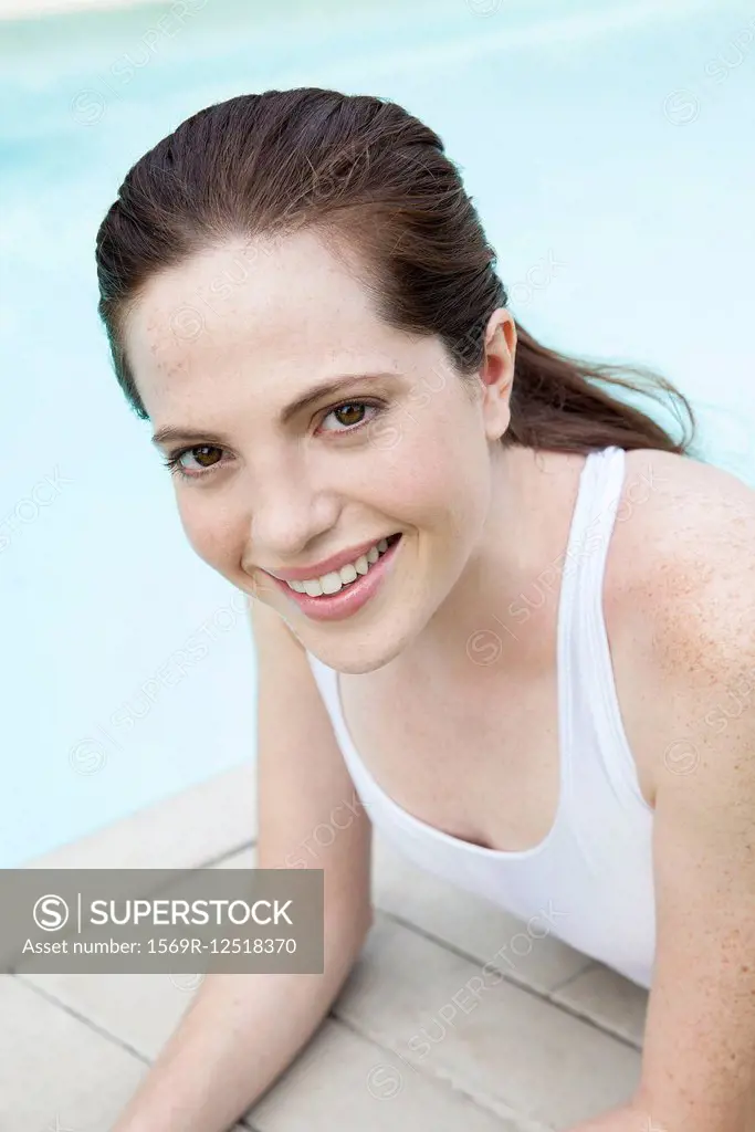 Young woman sunbathing by pool, smiling, portrait