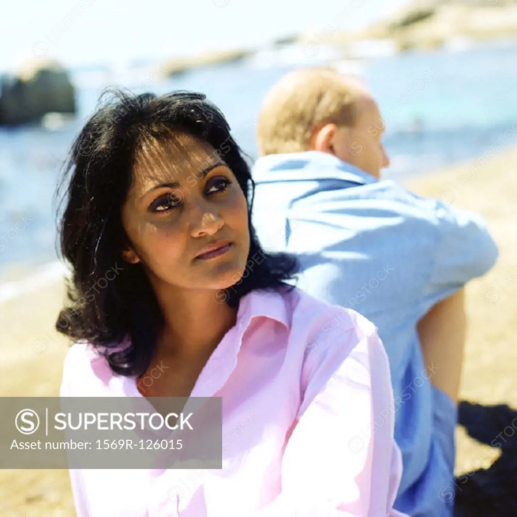 Couple sitting back to back on beach, focus on woman