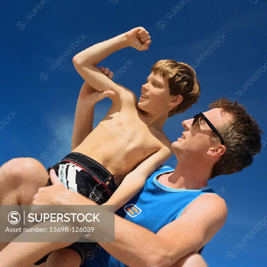 Father holding son, boy flexing arm, low angle view