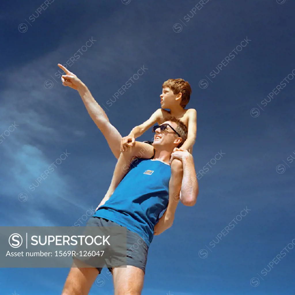 Boy sitting on man´s shoulders, man pointing, outside, low angle view