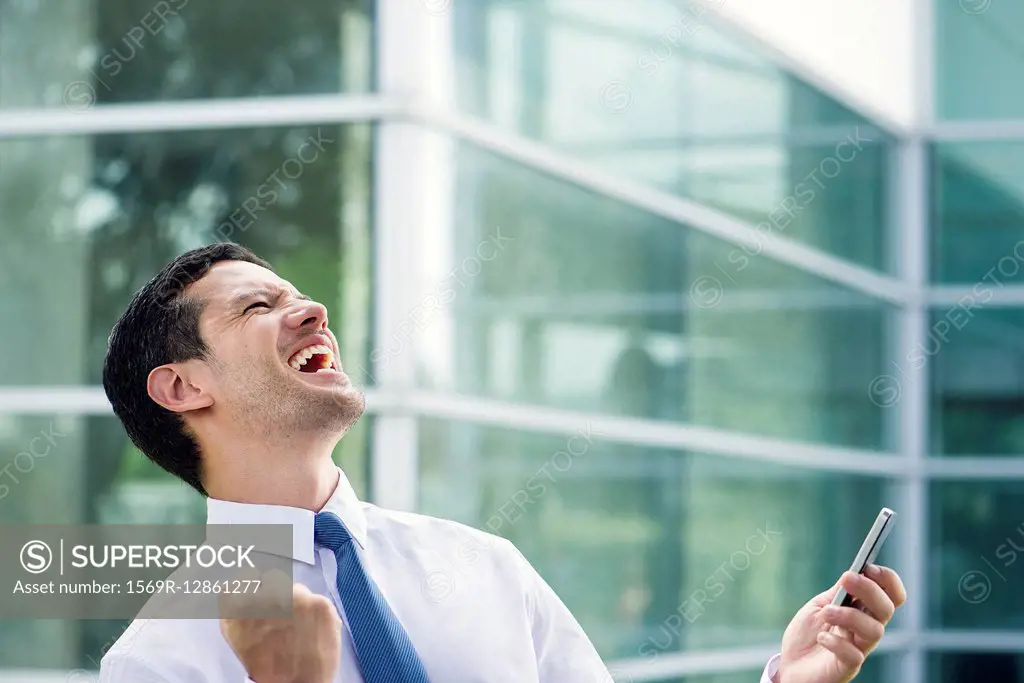 Businessman holding cell phone and celebrating good news