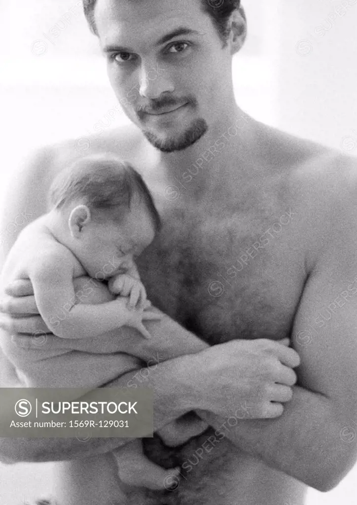 Topless father holding sleeping infant, looking at camera, b&w