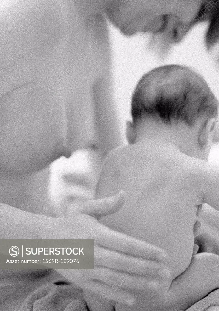 Nude mother patting infant on back, b&w