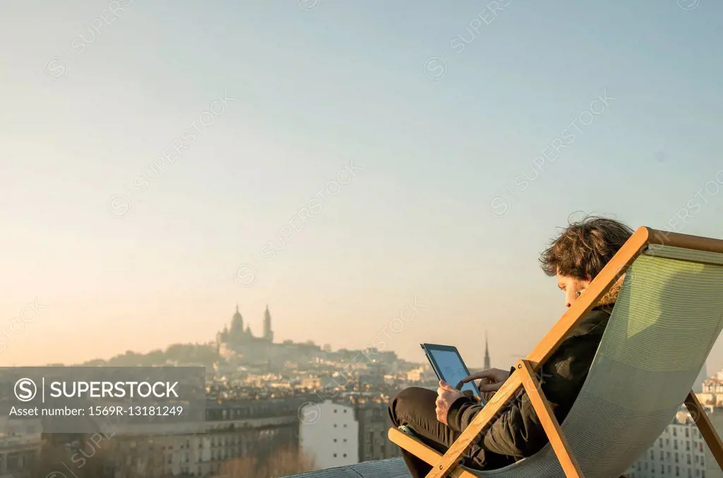 Man relaxing on rooftop terrace with digital tablet