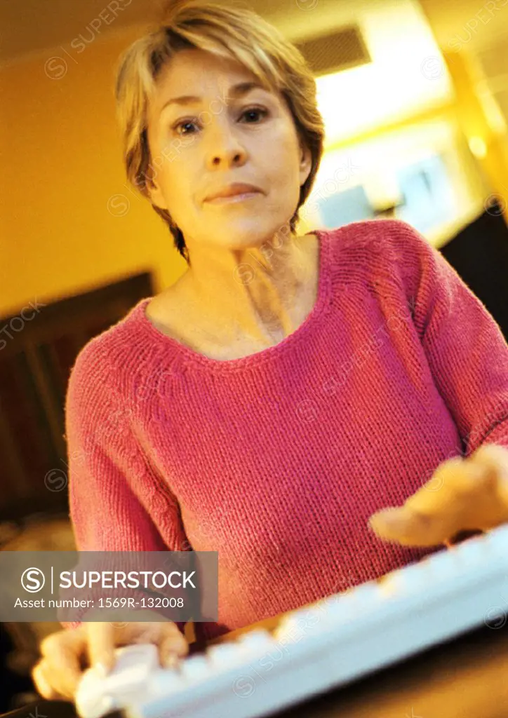 Mature woman, hands on computer keyboard, looking into camera, portrait