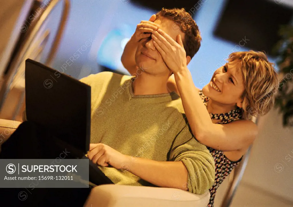 Couple, man using laptop, woman covering man´s eyes from behind