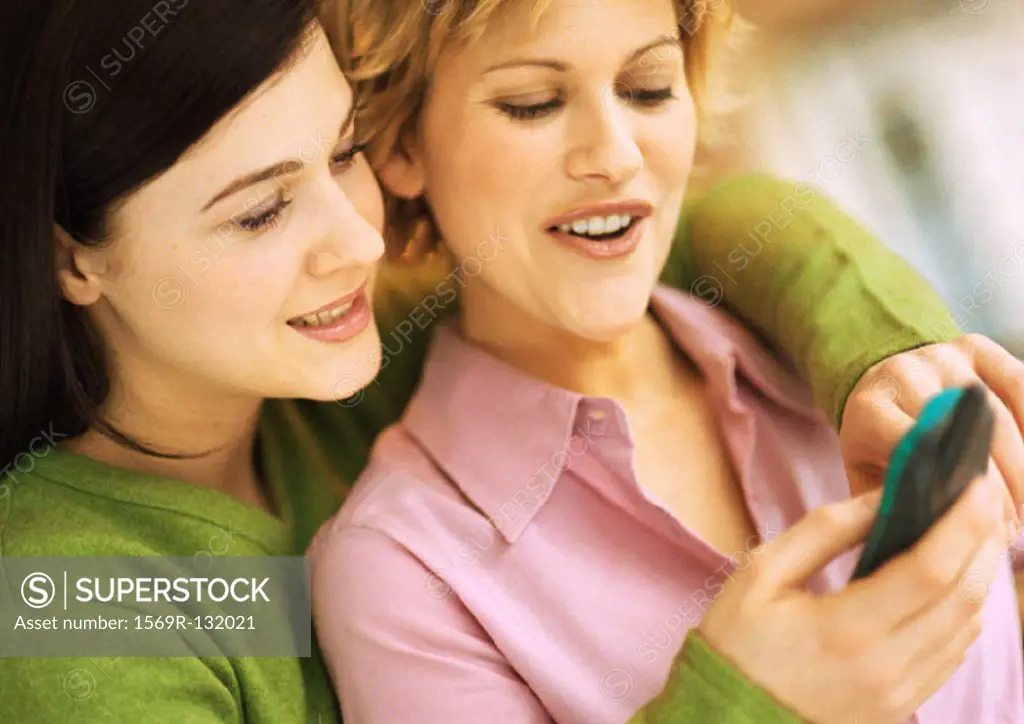 Two young women, one with arms around other, using cell phone, portrait