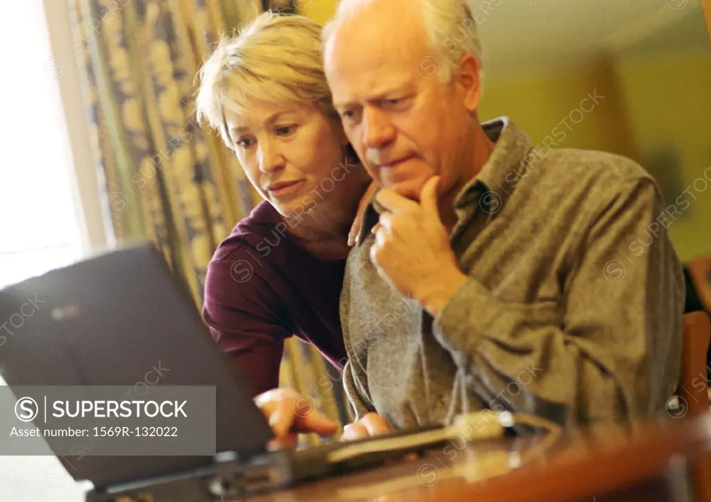 Mature couple, man using laptop, woman looking over shoulder