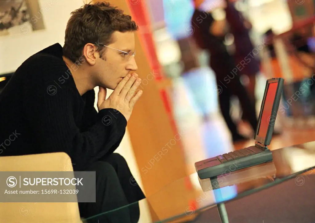 Man using laptop, hands in front of mouth, side view