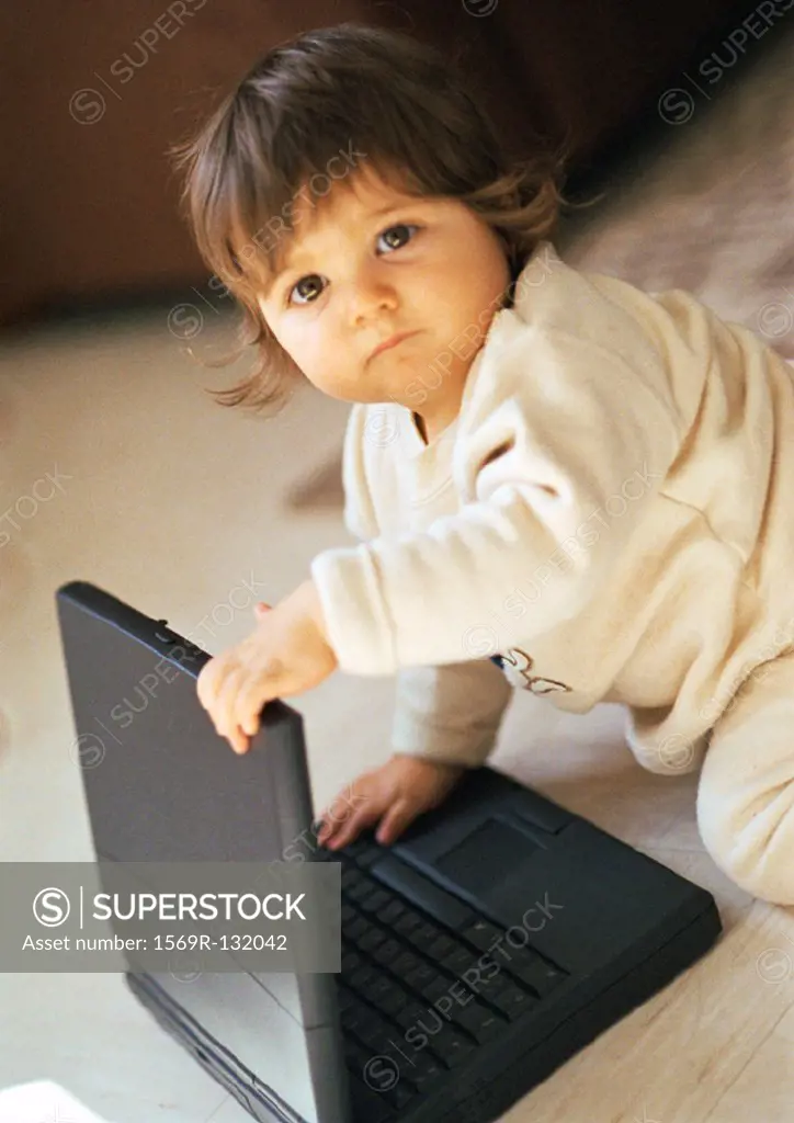 Baby playing with laptop, looking into camera, portrait