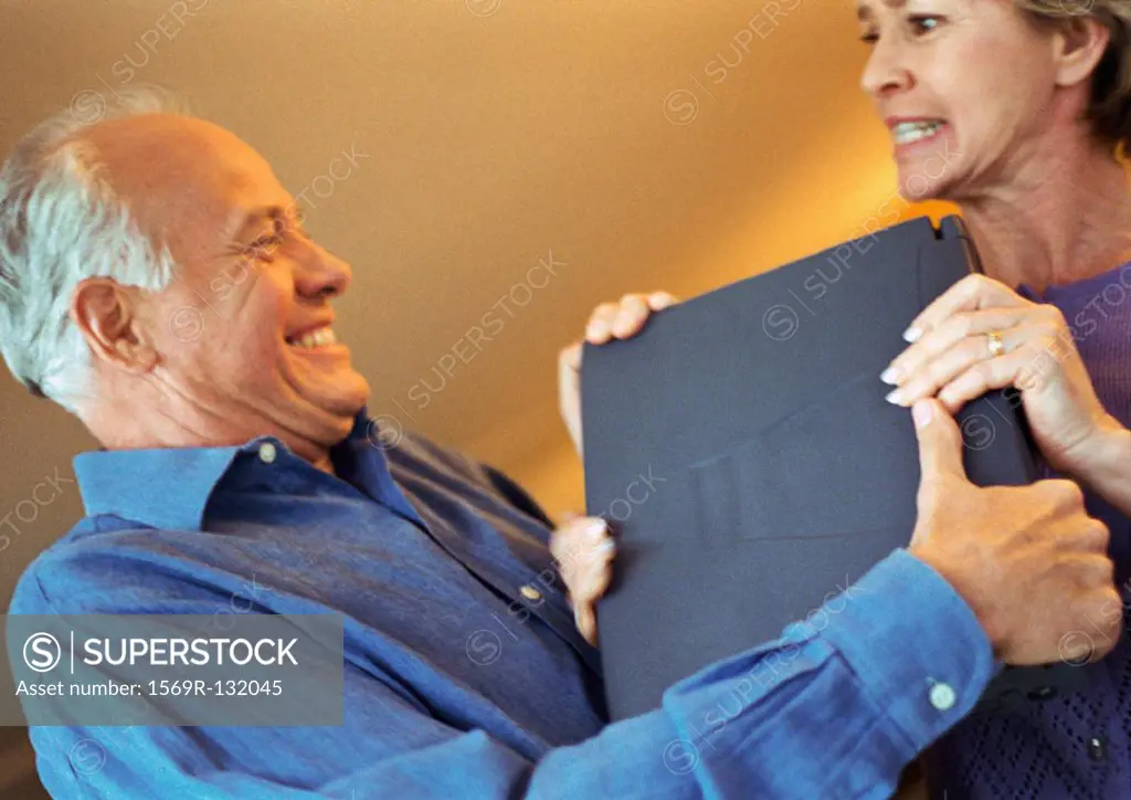 Mature couple fighting over laptop, portrait