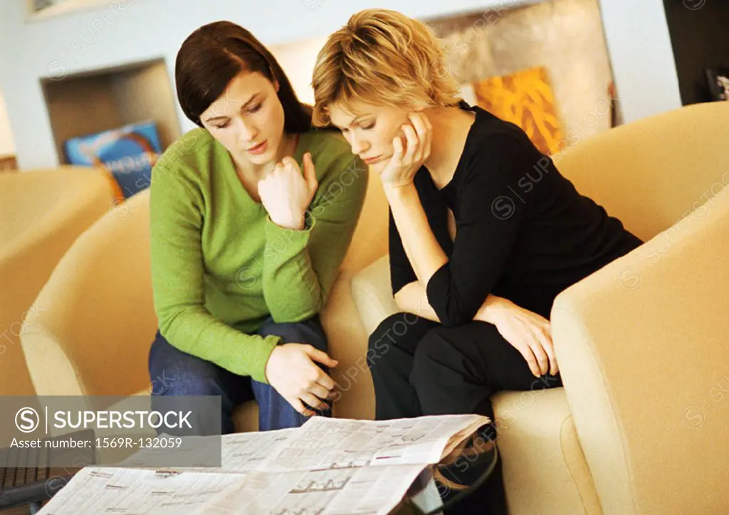 Two women sitting, reading newspaper