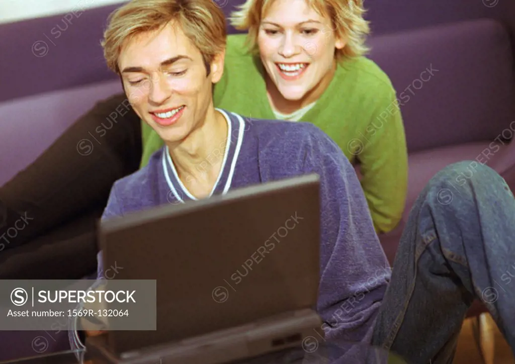 Couple smiling, man using laptop, woman sitting, looking over man´s shoulder