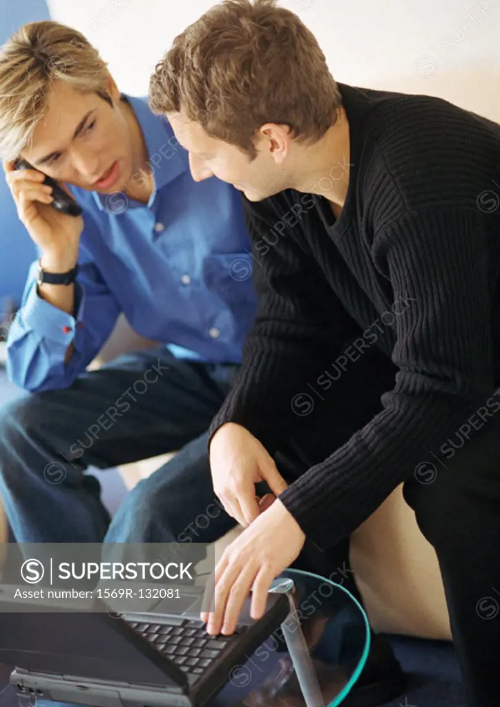 Two young men, one using laptop, one using cell phone