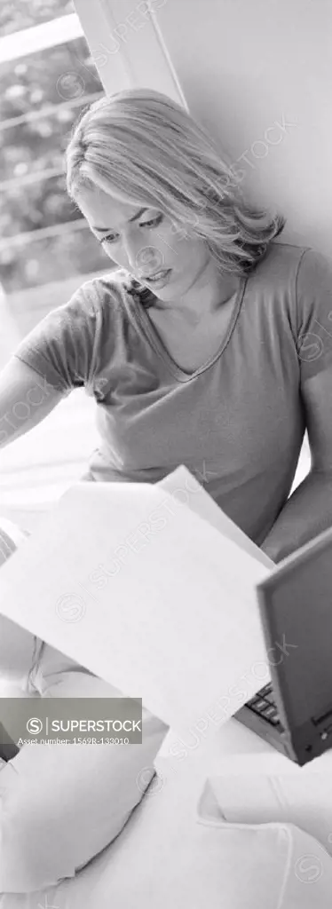 Woman lounging, looking at documents near laptop, b&w, vertical