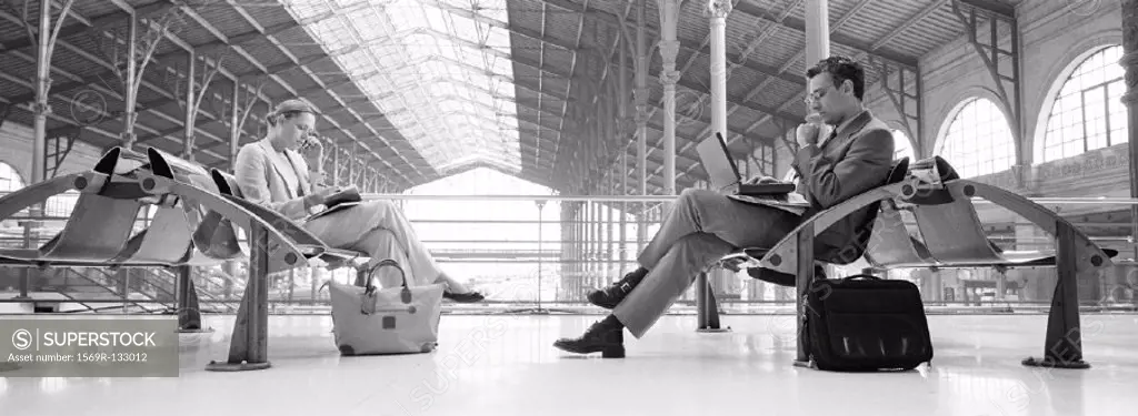 Businesspeople sitting in train station, b&w, panoramic view