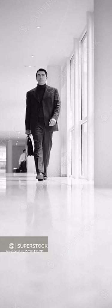 Businessman walking in hallway, b&w, vertical