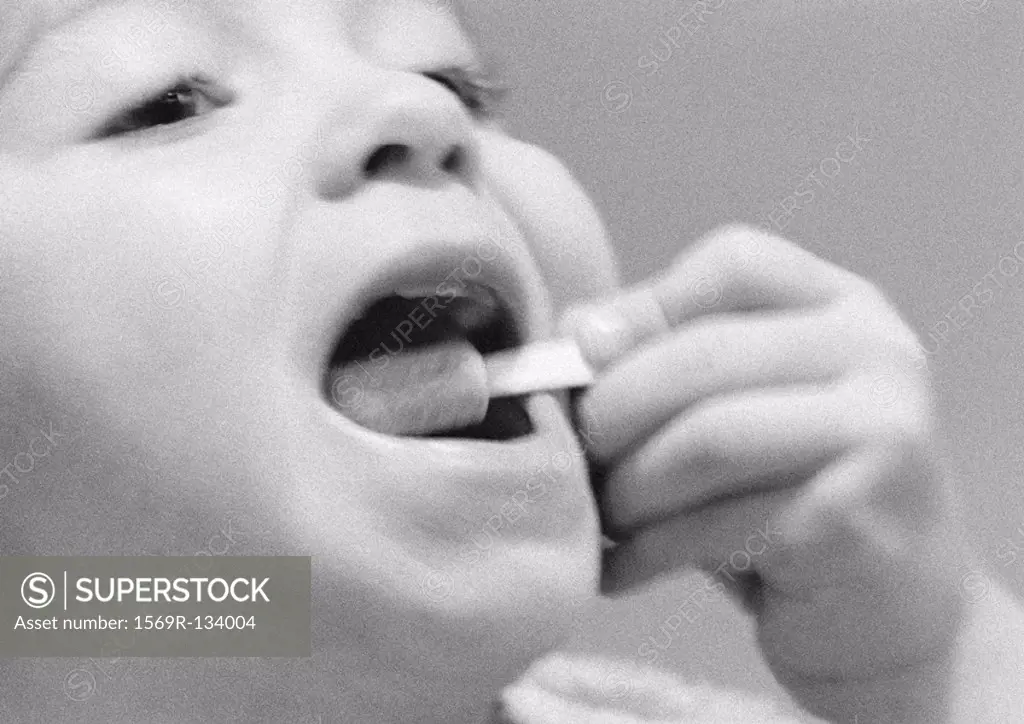 Young child putting something in mouth, close-up, b&w