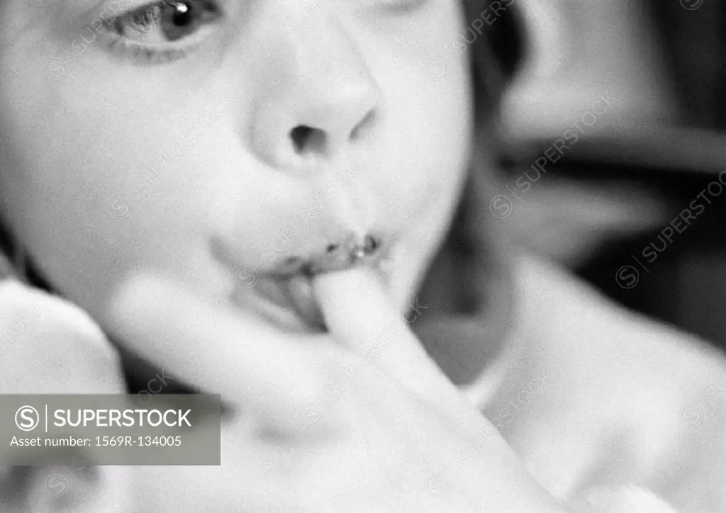 Young child eating, finger in mouth, close-up, b&w