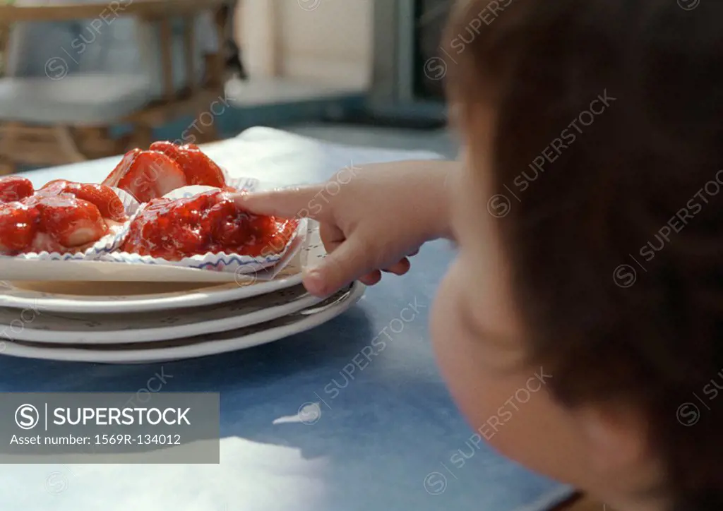Young child with finger on cake, focus on hand
