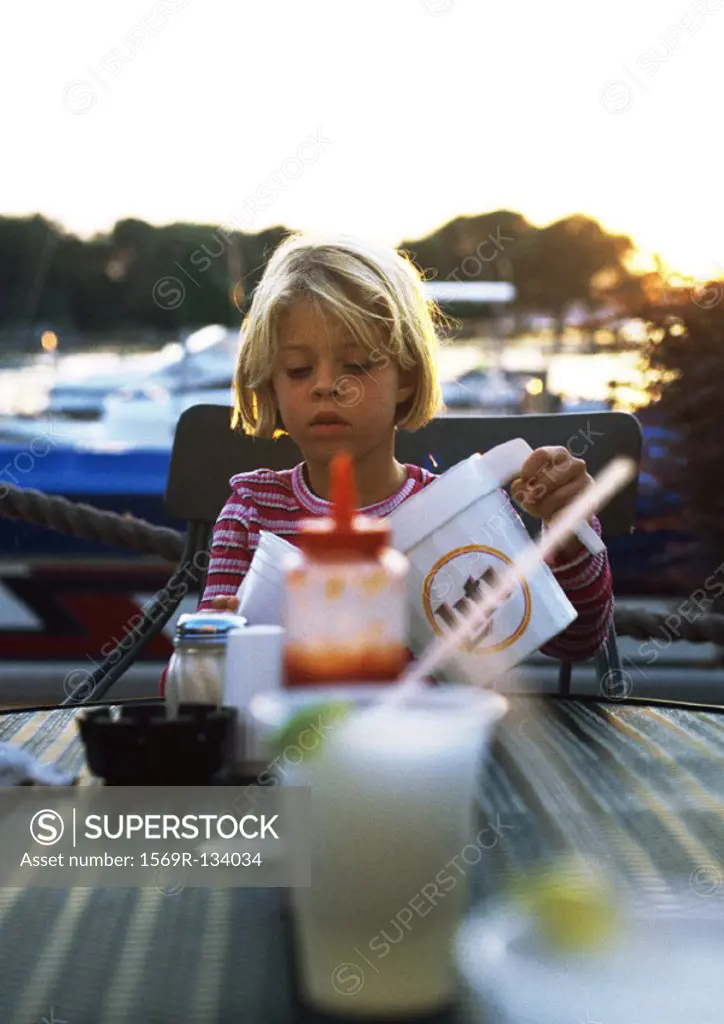 Child sitting at table, pouring drink