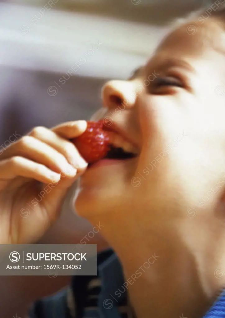 Young girl eating strawberry, laughing, side view, close-up