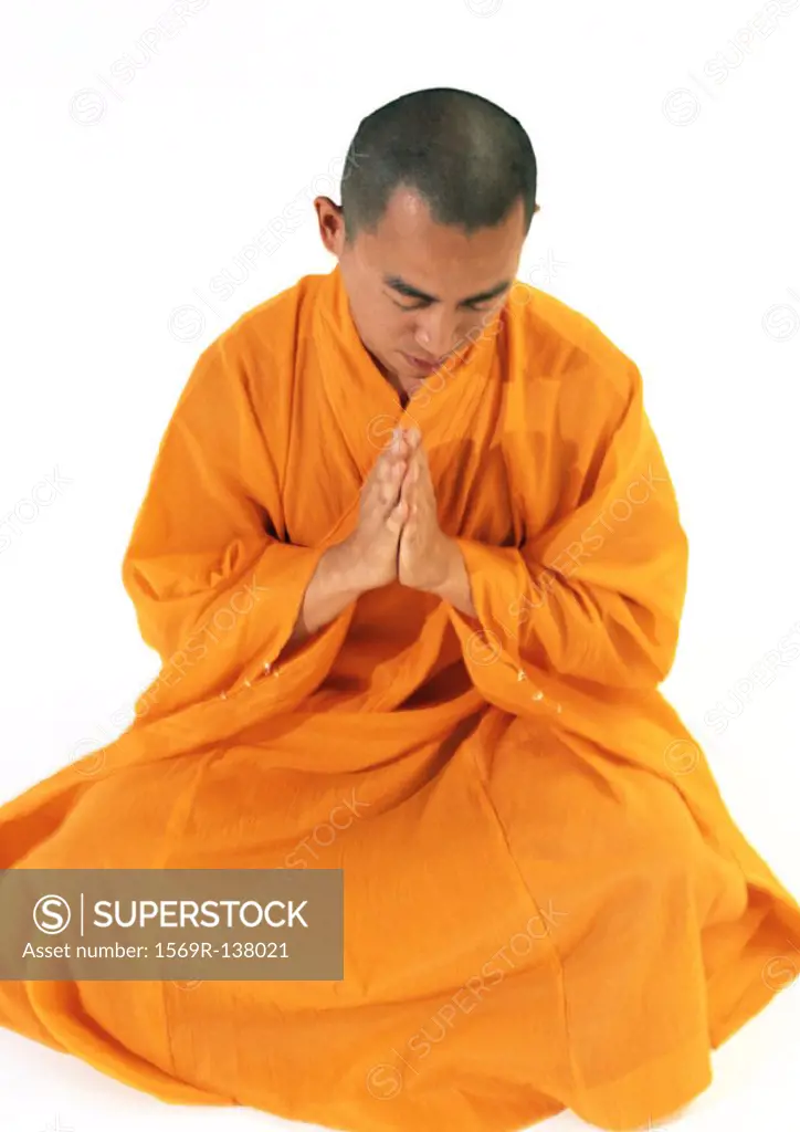 Buddhist monk sitting, meditating with hands together, high angle view