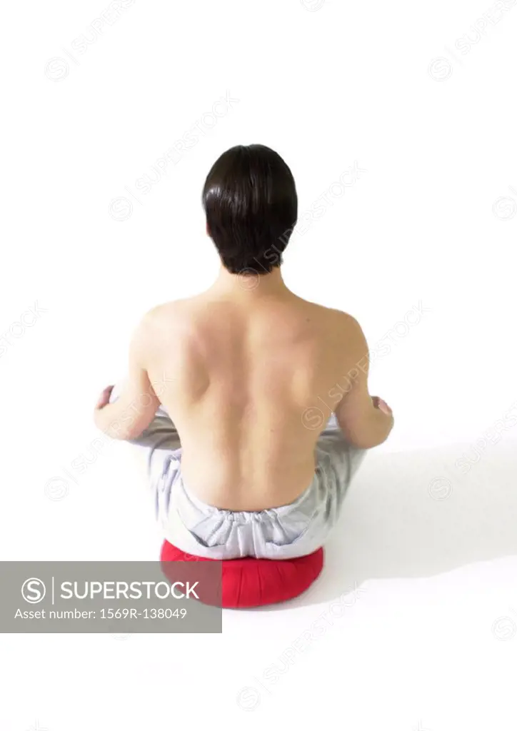 Topless man sitting on cushion, meditating, rear view