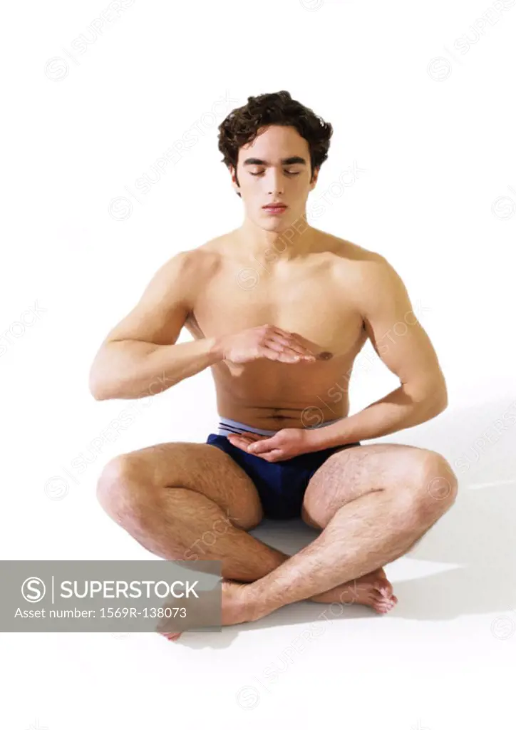 Man in underwear sitting indian style on floor with hands hovering in front  of torso - SuperStock