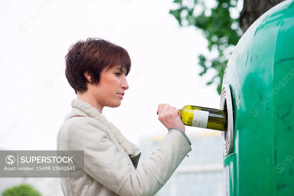 Woman putting wine bottle into recycling bin