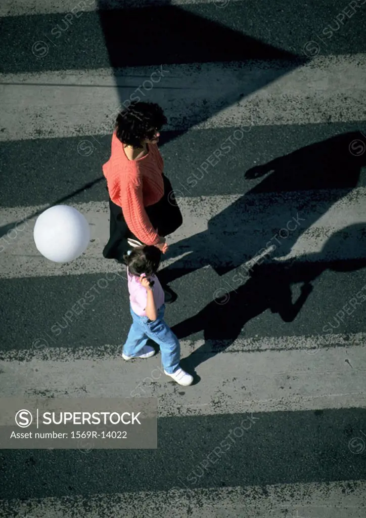Woman and young girl holding balloon, walking on crosswalk, high angle view