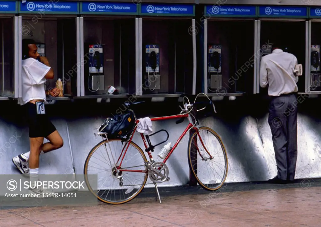 NY, NY, two men using pay phones, one with bike