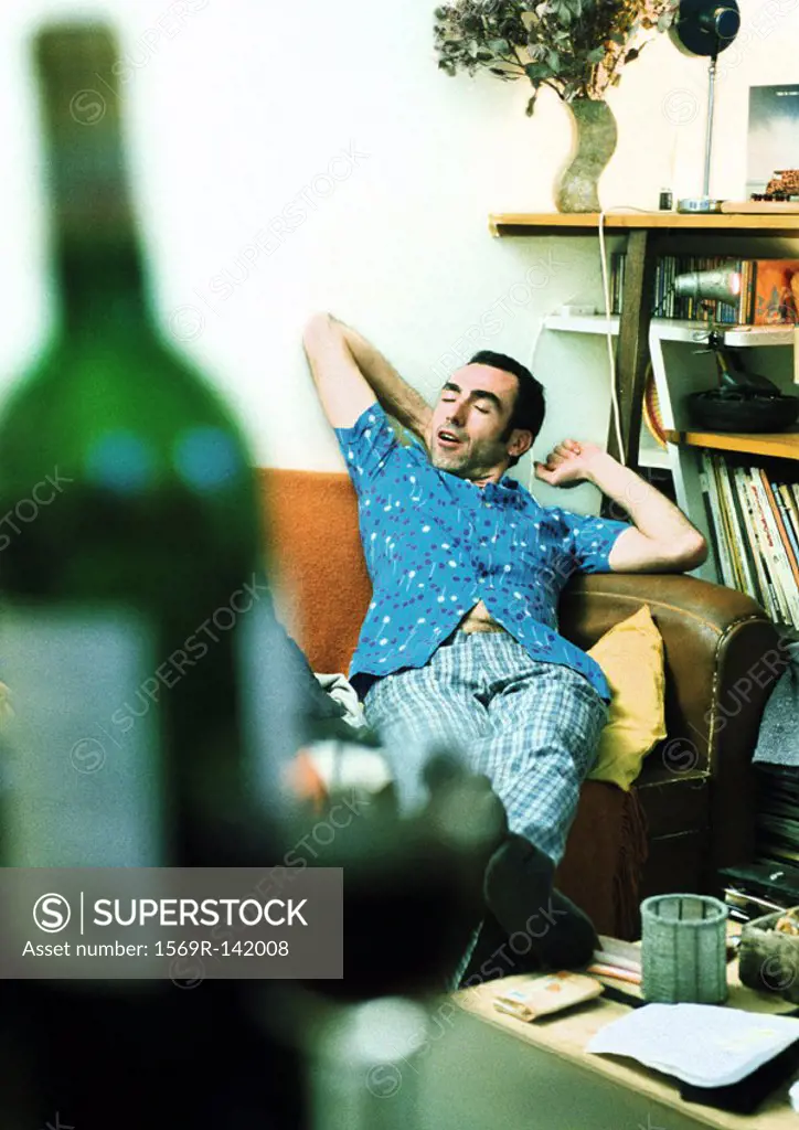 Man stretching on sofa, bottle of wine in foreground