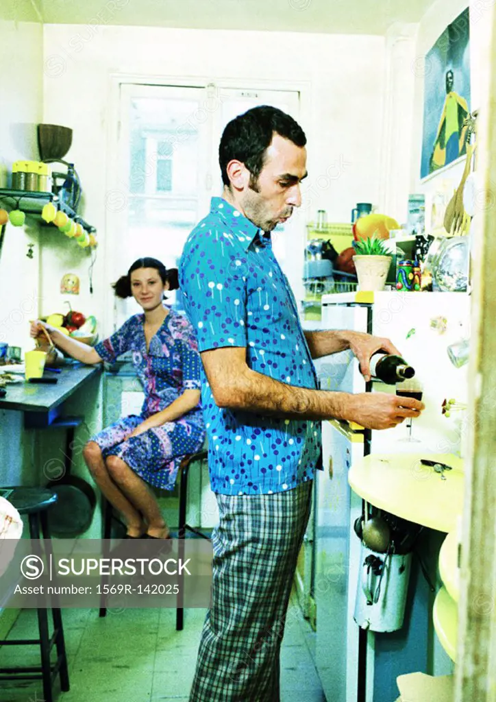 Couple in kitchen, woman sitting, man pouring wine