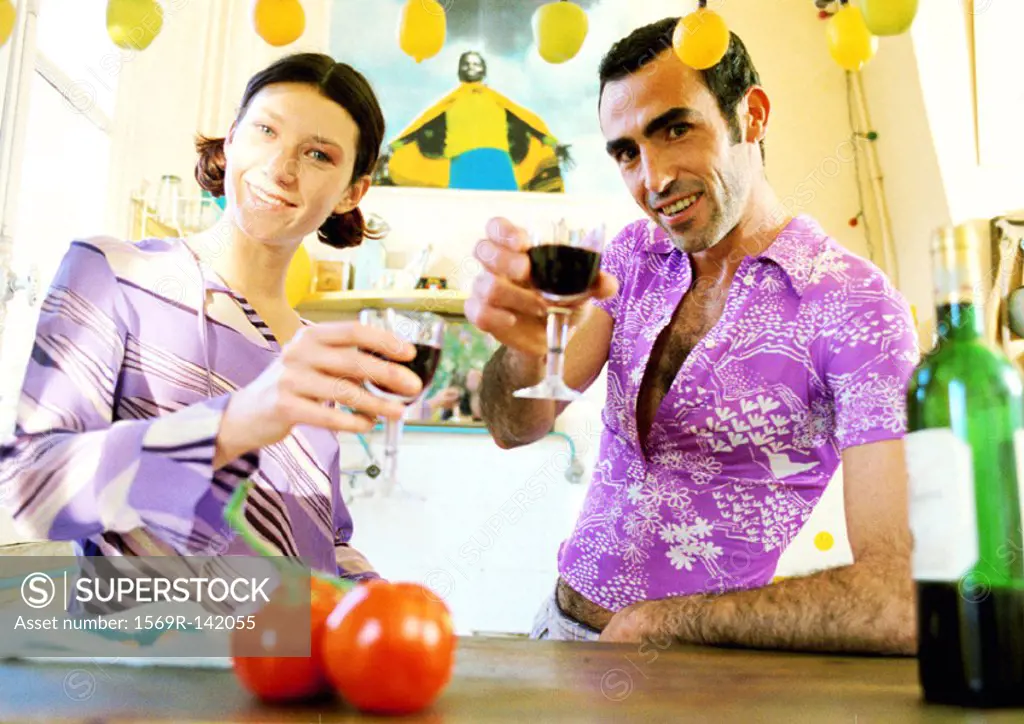 Couple standing in kitchen, raising their glasses