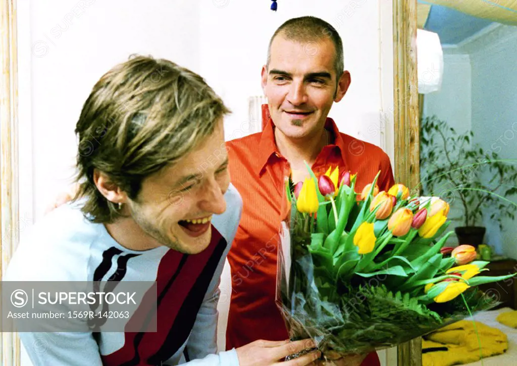 Two men smiling and laughing, one holding bouquet of flowers, portrait