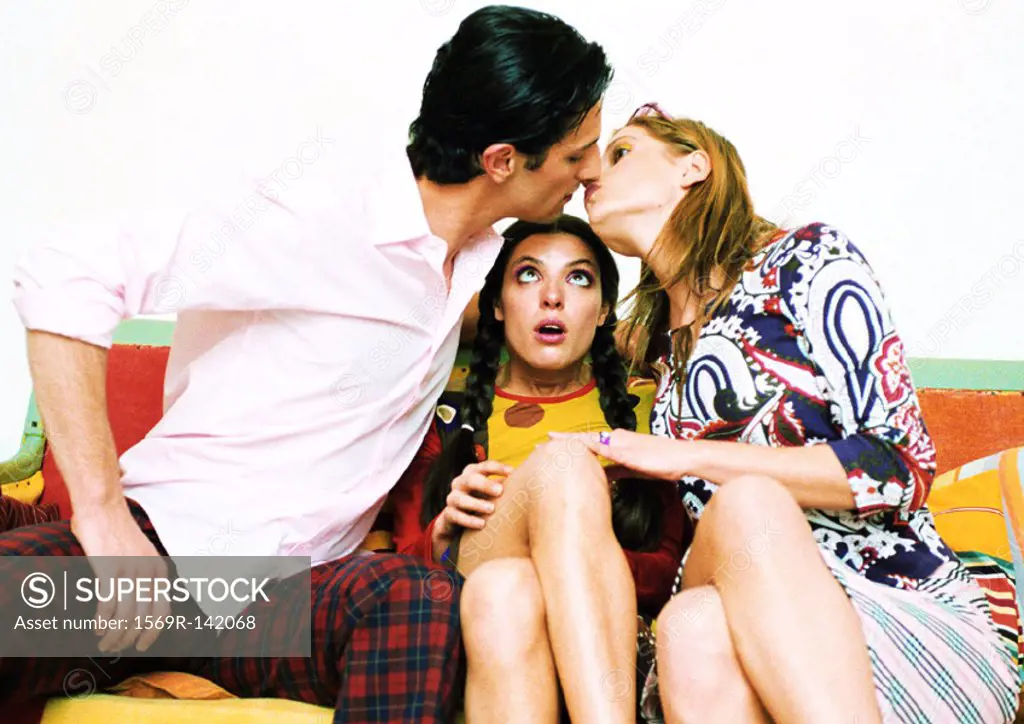 Young couple about to kiss, woman sitting between them watching