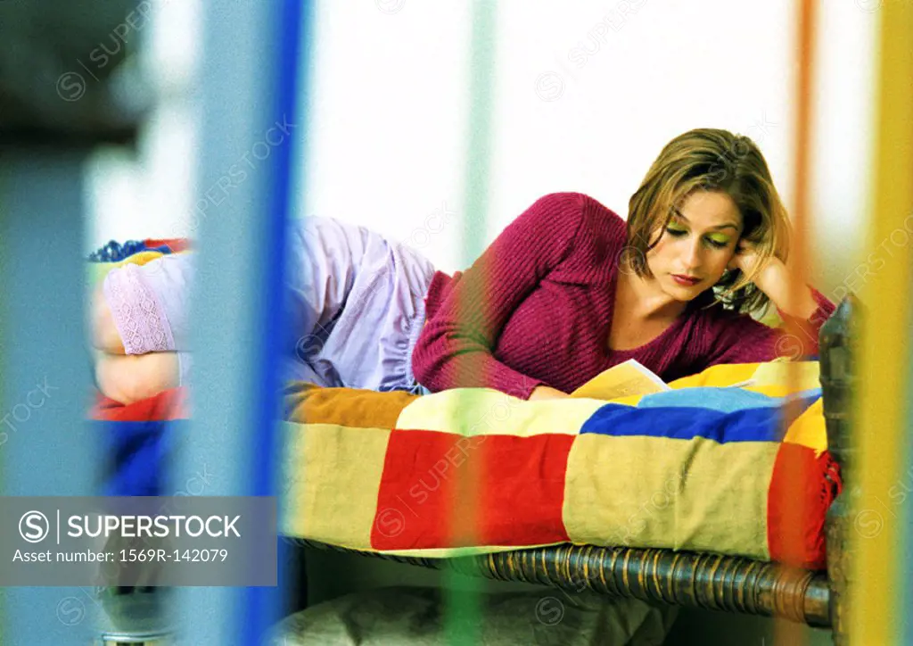 Young woman lying on bed reading