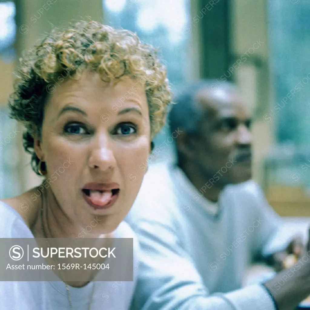 Woman sticking out tongue, man in background