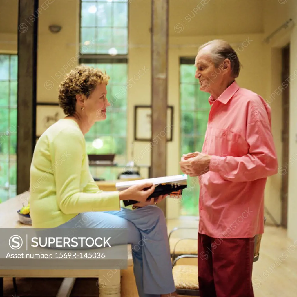 Mature couple face to face, woman sitting on table, man standing, side view