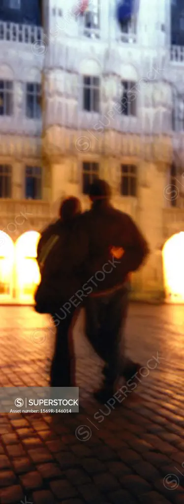 Couple walking with arms around each other at night, rear view, blurred
