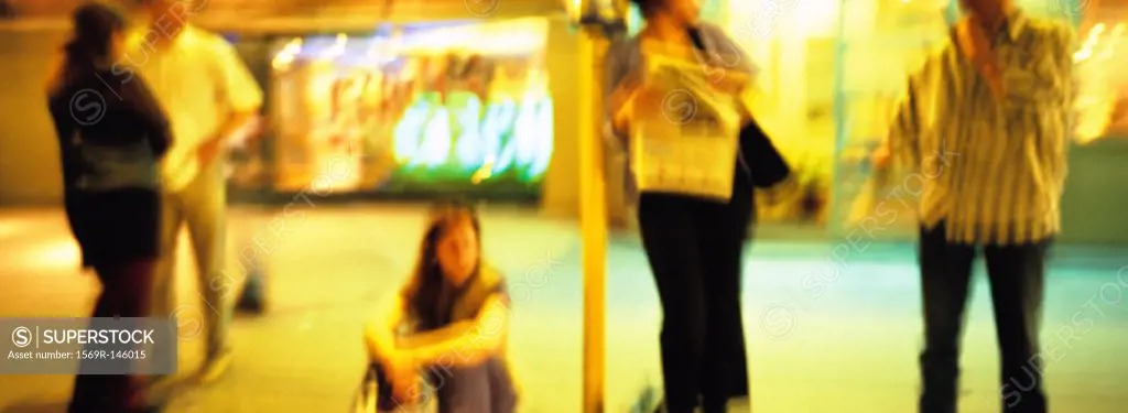 People waiting at bus stop at night, blurred
