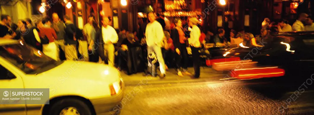 Crowd of people standing next to street, at night, blurred
