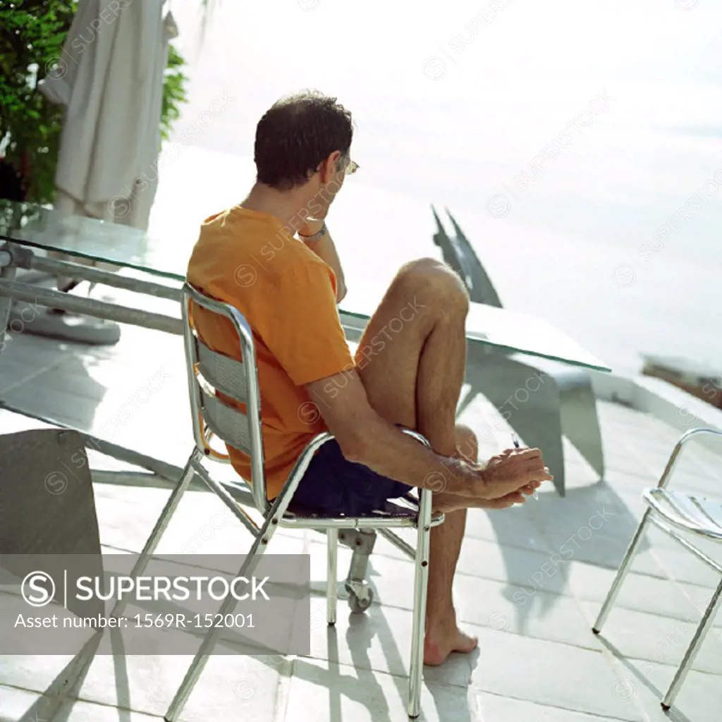 Mature man sitting, using phone, rear view