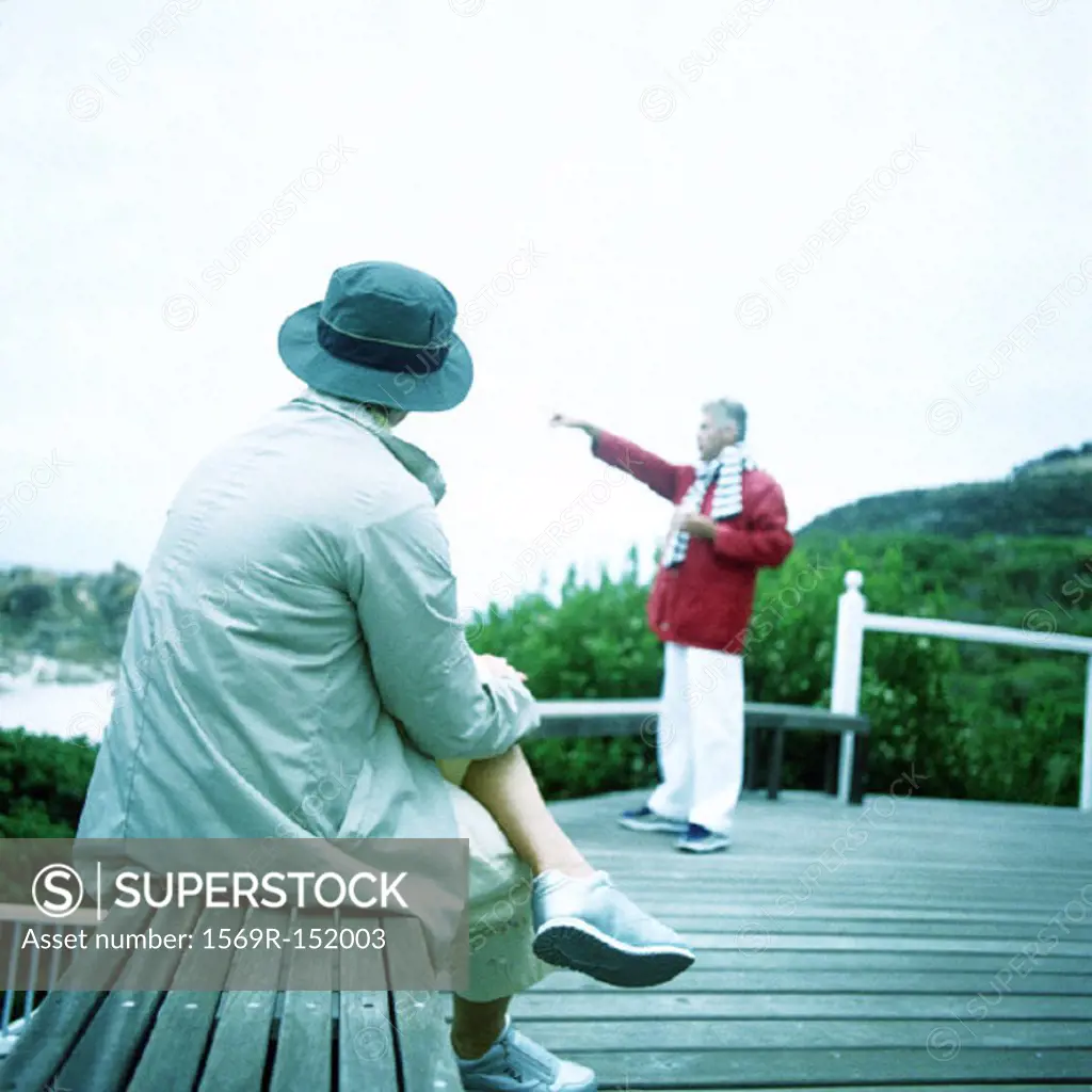 Mature woman sitting on bench, man pointing toward sea