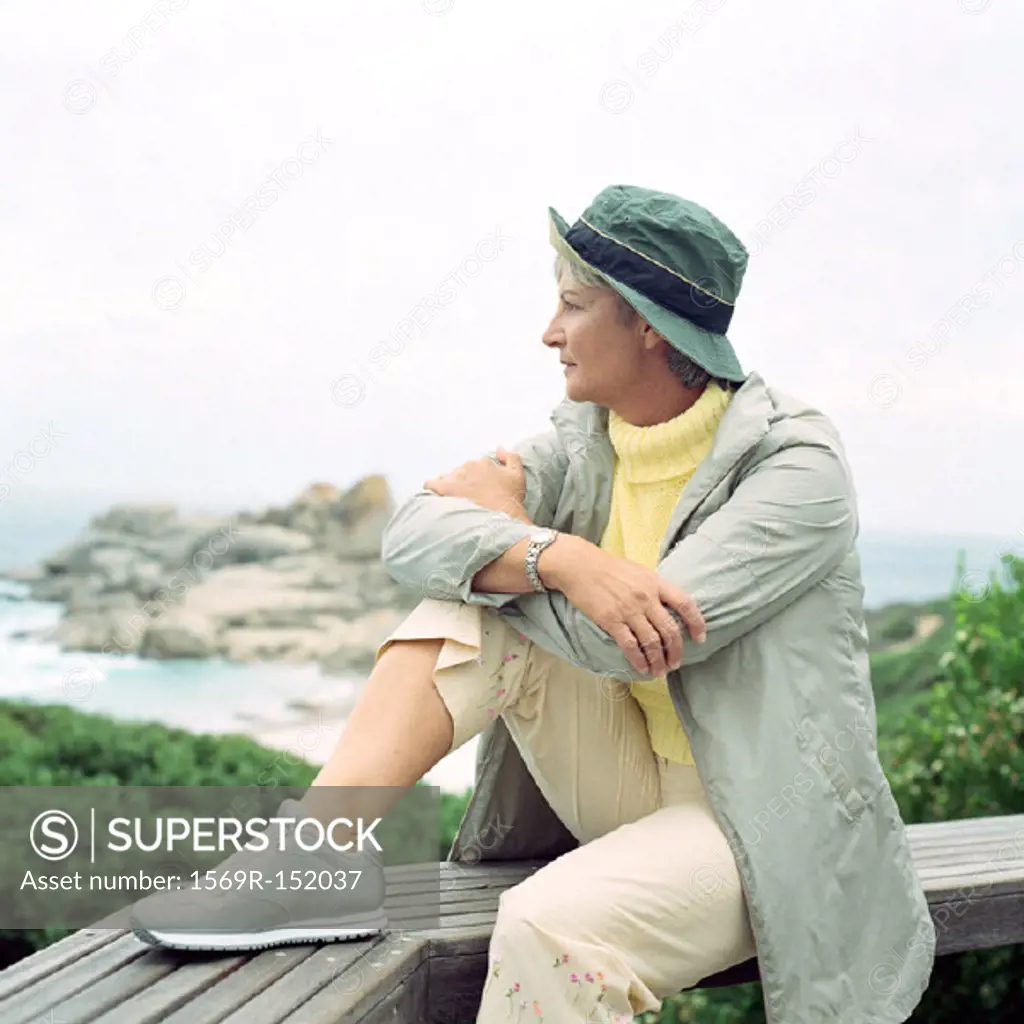 Mature woman sitting on beach, looking out to sea, side view, portrait