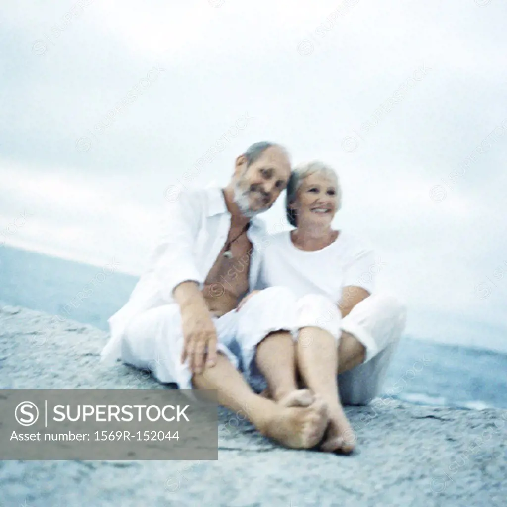 Mature couple sitting on beach, looking into camera