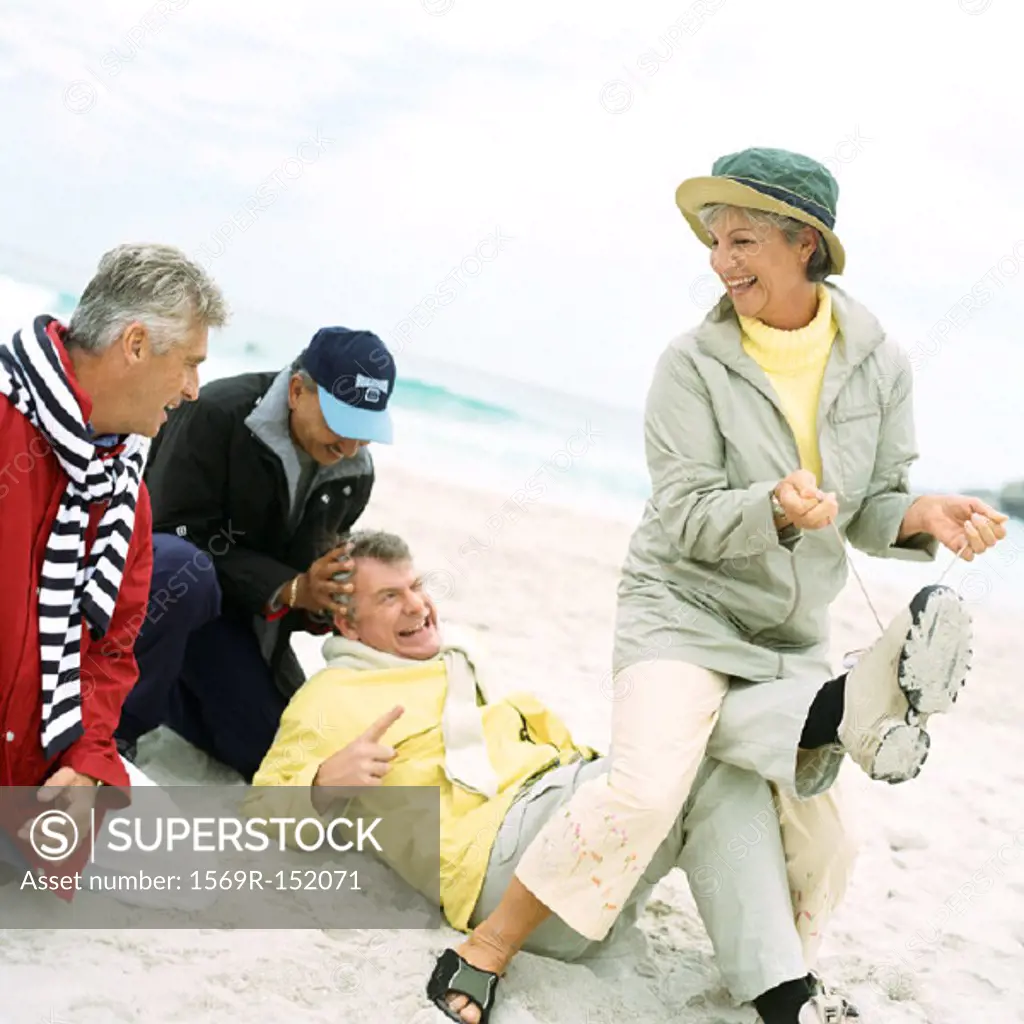 Mature group playing on beach, woman pulling man´s laces